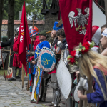 Grupa osób w strojach historycznych zebrana na kościelnym dziecińcu.