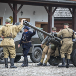 62. Trzech mężczyzn w wojskowych mundurach i jeden w mundurze policjanta stoją przy wojskowych samochodach na rynku miasteczka.