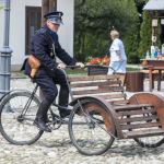 Mężczyzna w mundurze policjanta jadący rikszą przez rynek miasteczka.