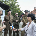 Kobieta z mikrofonem, przed nią mężczyźni w mundurach.