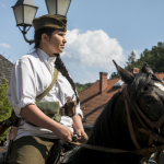 Siedząca na koniu kobieta w białej koszuli i ciemnozielonej czapce