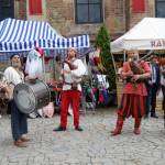 Zespół muzyki dawnej grający na instrumentach na kościelnym placu, z tyłu stoiska.