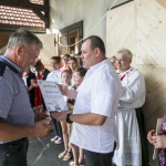 Mężczyzna wręcza innemu mężczyźnie dyplom, obok ludzie stojący na scenie.