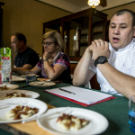 Dwóch mężczyzn i kobieta siedzący za stołem z jedzeniem i napojami.