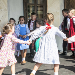 Trzymające się za ręce, tańczące przed budynkiem dzieci.