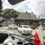 Zabytkowe auta widziane przez szybę samochodu, zatknięta w środku biało-czerwona flaga.