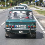 Ciemnozielony samochód widziany od tyłu jadący jezdnią.