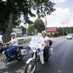 Kobieta i mężczyzna na białych motocyklach z napisem Milicja, na szosie, z tyłu auto.