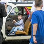 Chłopiec za kierownicą samochodu, przed nim obrócone tyłem trzy osoby