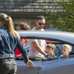 Kobieta chwytająca za klamkę samochodu, za autem mężczyzna i dwóch chłopców.