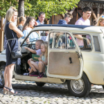 96. Dzieci wewnątrz auta, naprzeciwko kobieta, za autem ludzie.