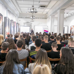 15. Siedząca tyłem publiczność, na ścianach obrazy.