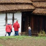 Kobieta, mężczyzna i dziewczynka idą do drewnianej chaty.