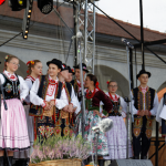 Młodzież w strojach regionalnych zgromadzona na scenie.