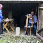 Mężczyzna struga łyżki na tokarce, czynności przygląda się dziewczyna i chłopak.