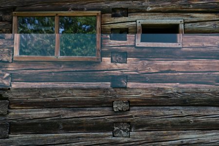 Okno w ścianie drewnianej chaty, obok małe okienko.