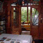 Drewniane brązowe drzwi, stół nakryty białym obrusem, w kącie regał z książkami, na ścianie obraz, w tle kot na stoliku.