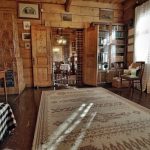 Drewniana izba, na podłodze leży dywan, drewniane drzwi.