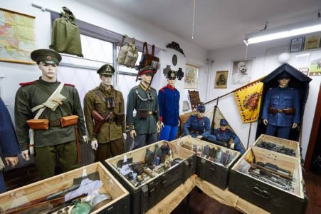 Manekiny ubrane w żołnierskie mundury, na ścianach wiszą plecaki i obrazy, w skrzynkach wojskowe akcesoria.