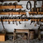 Na bielonej drewnianej ścianie kilka półek z różnorakimi narzędziami gospodarstwa domowego.