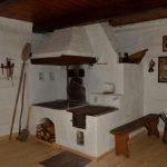 Bielony piec w rogu chałupy. Obok ławka.