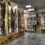 Narty i zdjęcia ustawione w gablotach w sali muzealnej.