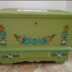 Zielona skrzynia drewniana, malowana na zielono, i w kwiaty.