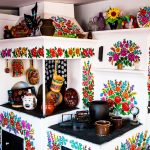 Biała kuchnia, ozdobiona kolorowymi kwiatowymi wzorami, na kuchni stoją naczynia.