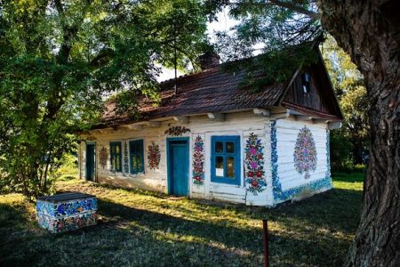 Bielony, zdobiony malunkami kwiatów, drewniany dom.