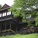 Zabytkowa, drewniana brązowa willa, pośród zieleni.