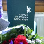 Ciemnozielona okładka a na niej napis nagroda im. Mariana Korneckiego, przed nią leżący na stole bukiet kwiatów .