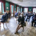 Kilkanaście osób siedzących na krzesłach na sali konferencyjnej.