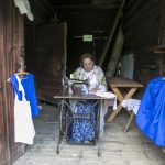 Kobieta w stroju ludowym szyje na dawnej maszynie do szycia.